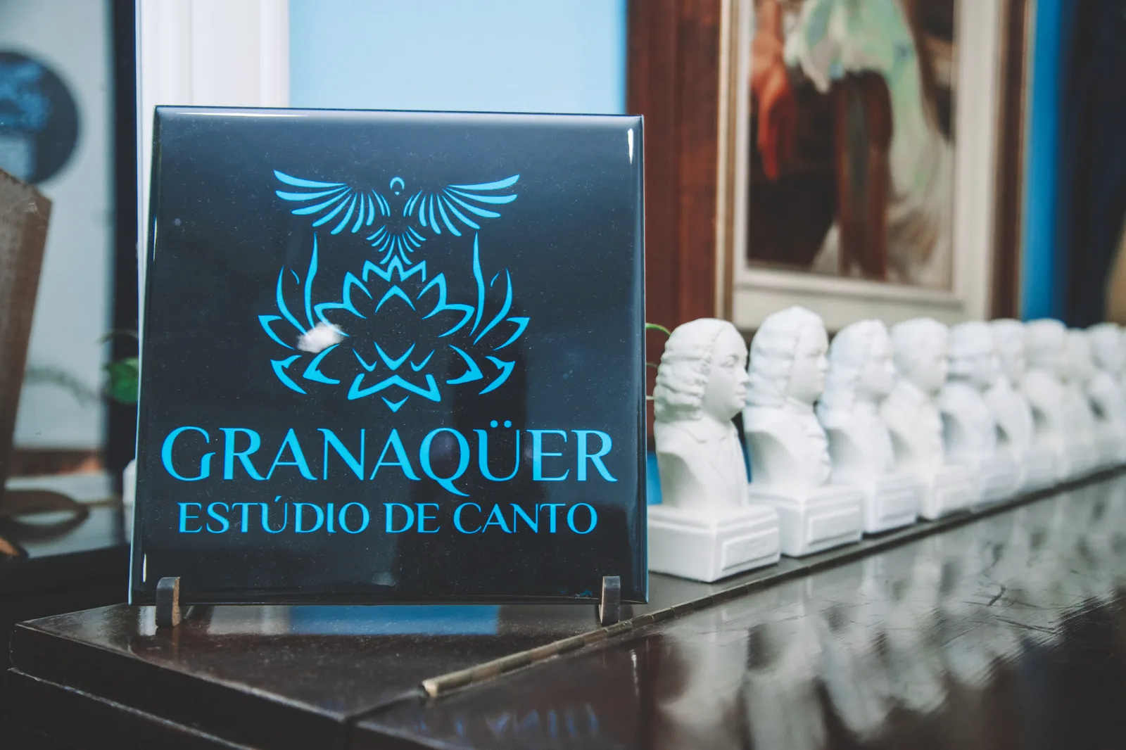 Placa com o logotipo Granaqüer Estúdio de Canto ao lado dos bustos de compositores sobre o piano
